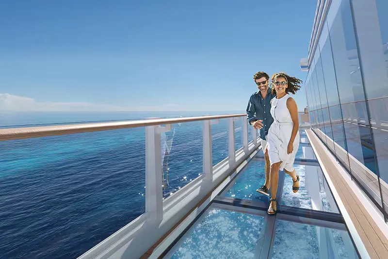 Casal caminhando em passarela de vidro junto ao mar